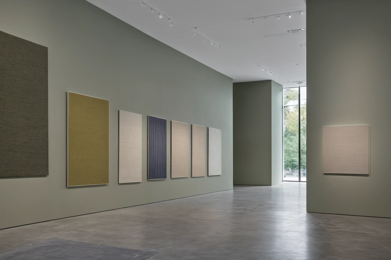 Museum gallery wall hung with large framed flat-woven wool textile panels in a tall exhibition space